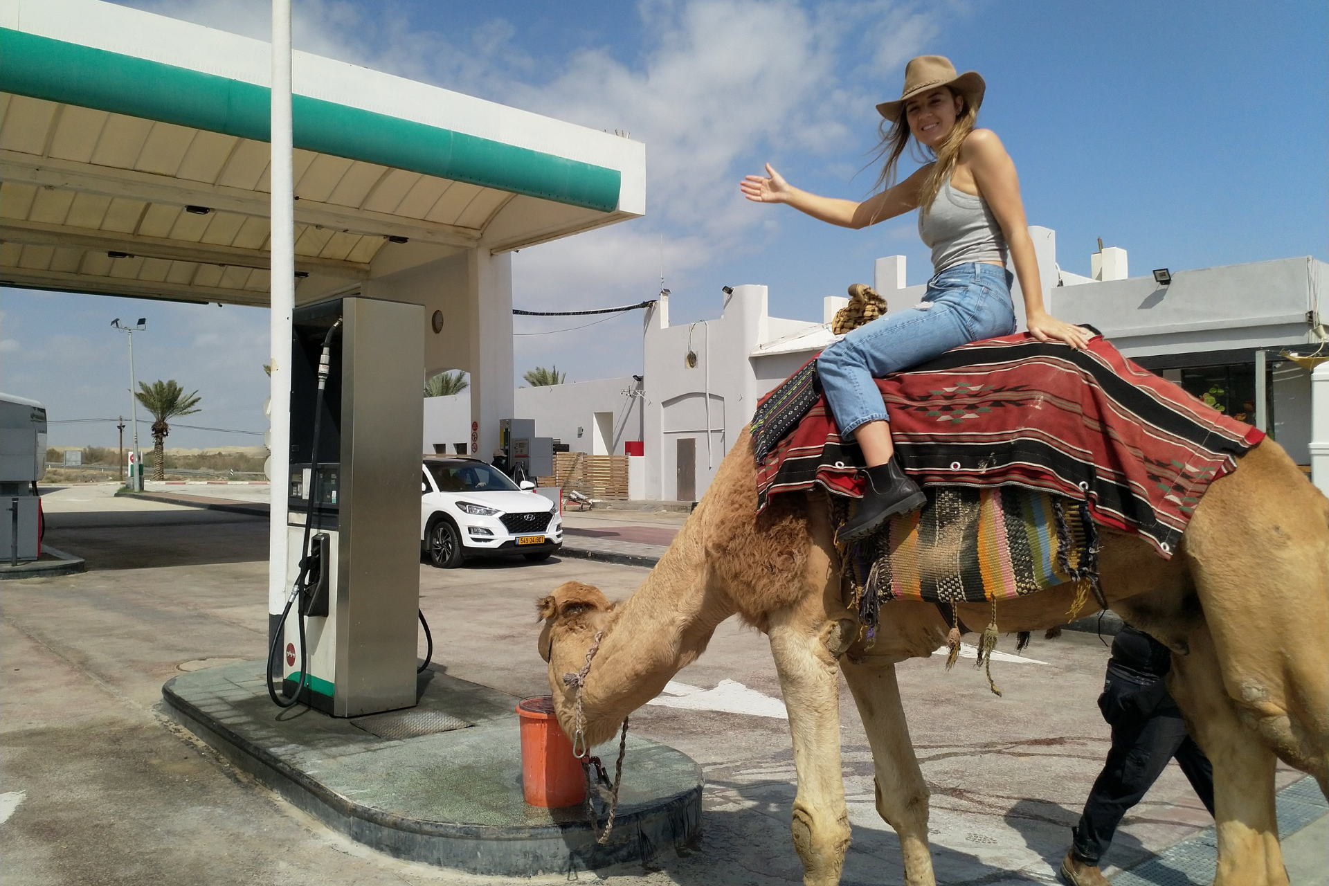 Ezra Traveler Riding a Camel to a Gas Station with Camel Drinking Water